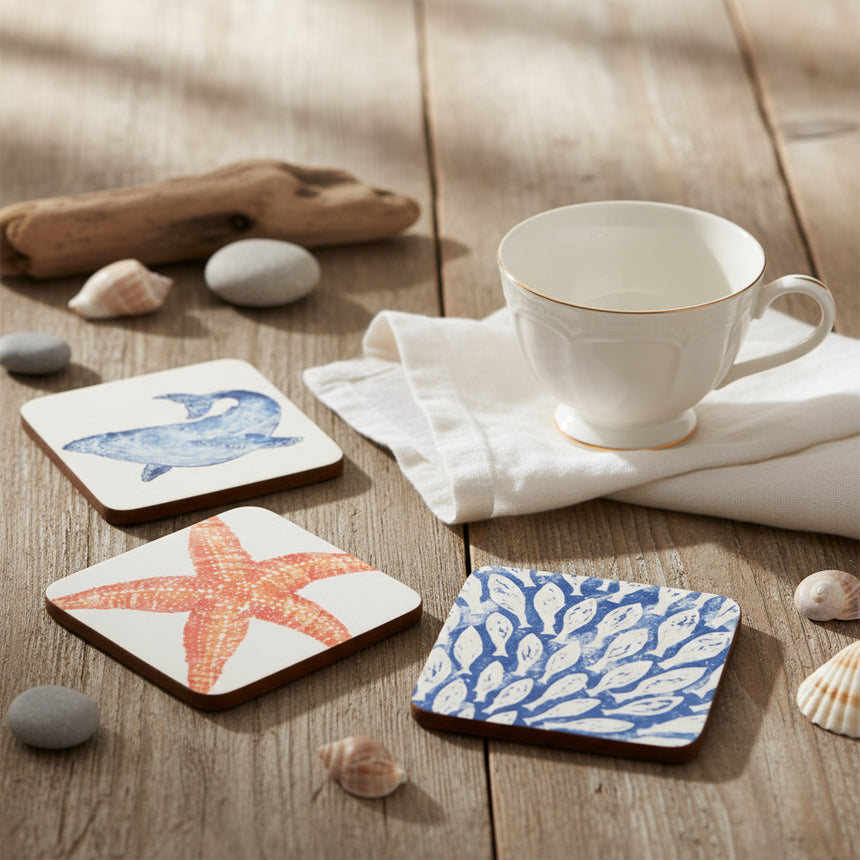 A set of four square coasters with sea life illustrations including a whale, an octopus, a starfish, and a fish shoal on a white background.