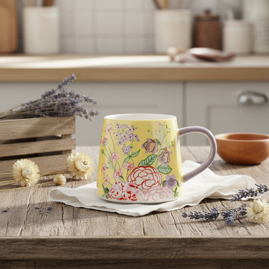 A ceramic mug with a yellow base and a floral pattern featuring various flowers and a butterfly, with a contrasting pastel handle.