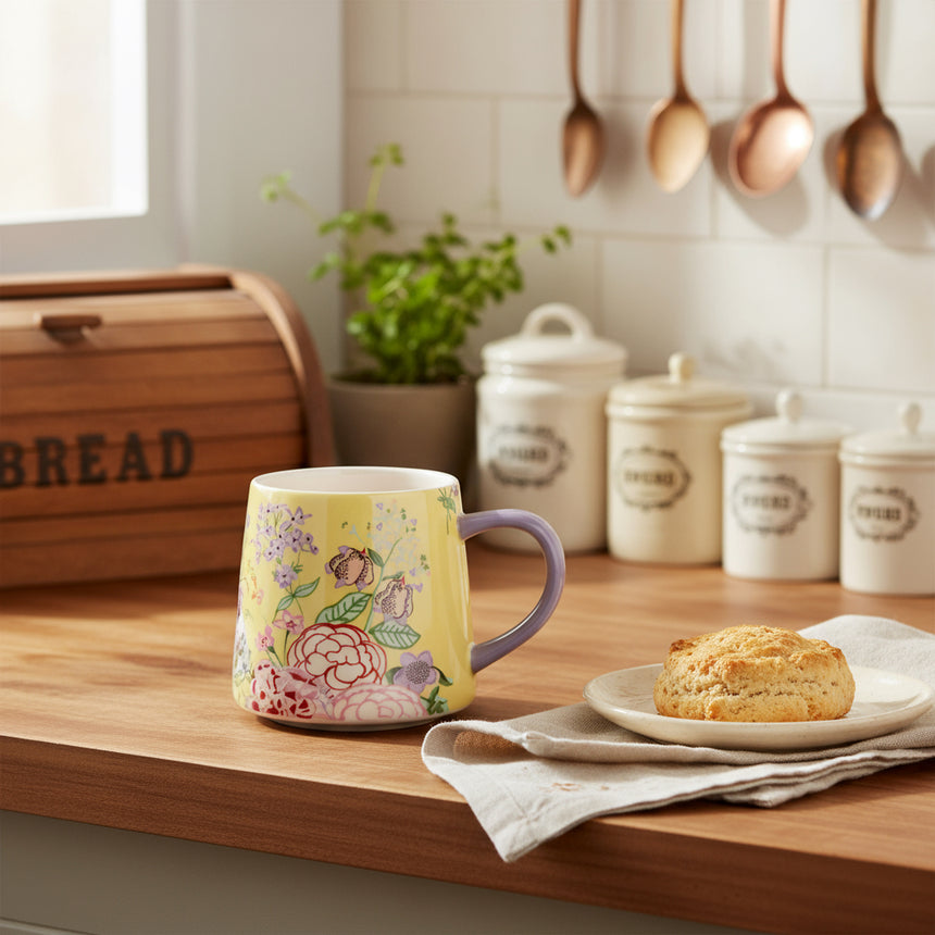 Yellow mug with floral design and purple handle on a white background