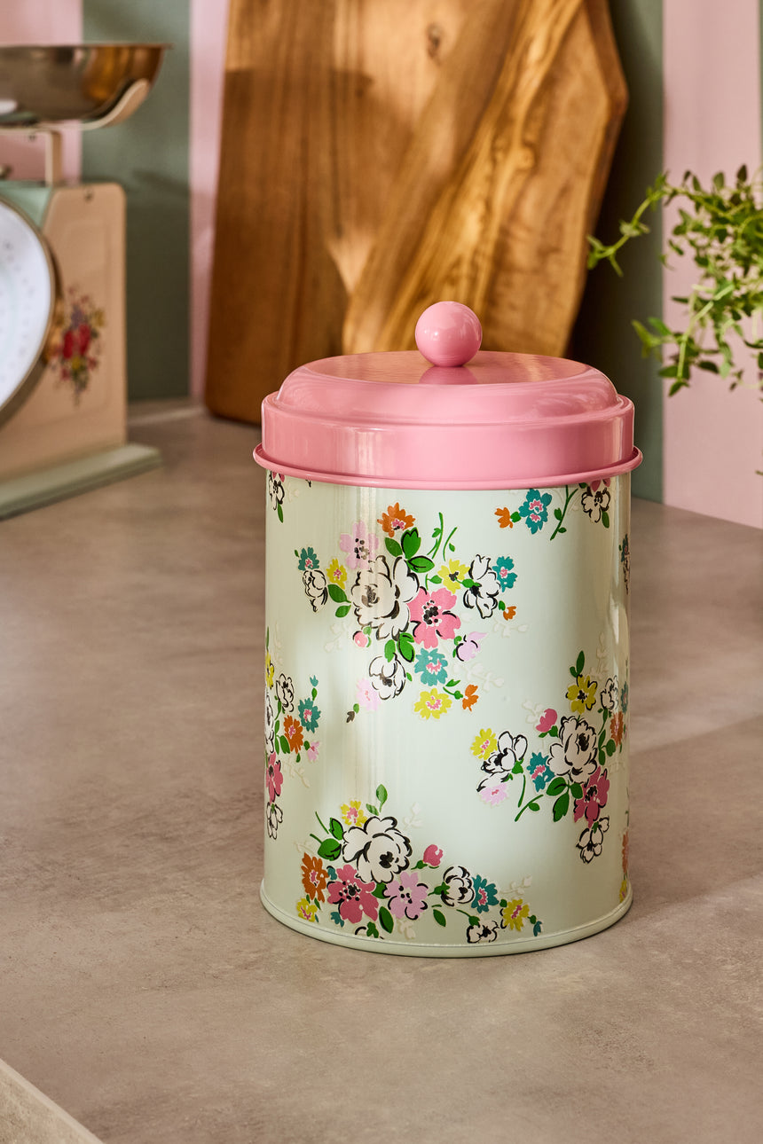 Decorative storage canister with floral design and pink lid on a wooden floor.