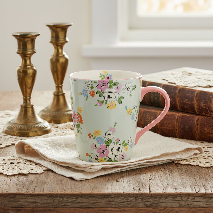 A ceramic mug with a floral print design featuring pastel pinks, blues, yellows and greens, and a pale pink handle.