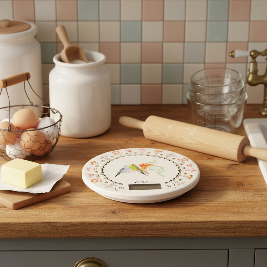 A digital kitchen scale with a floral and bird design on a white background, with a digital display and pink edging.