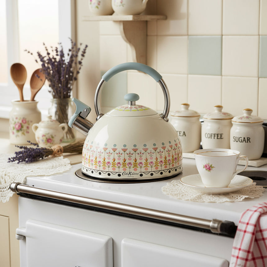 A cream-colored stovetop kettle with a floral pattern and a blue handle, part of the Cath Kidston Painted Table range.