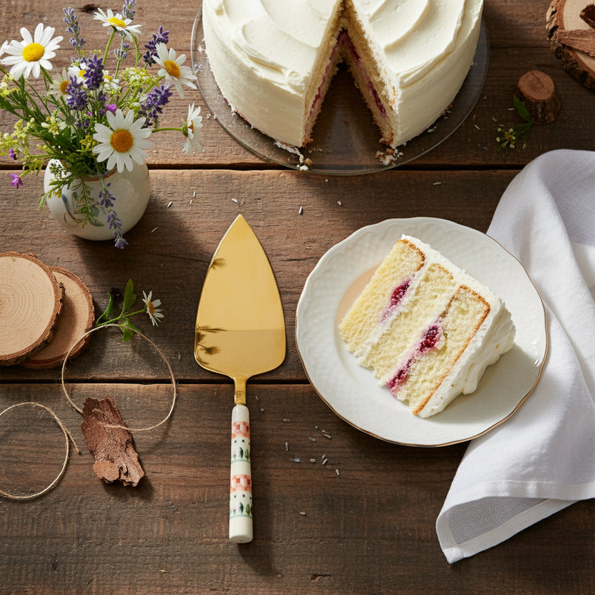 Gold cake server with a patterned handle on a white background