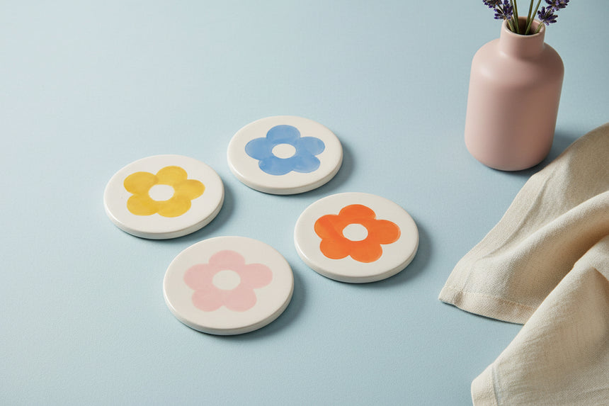 A set of four round ceramic coasters, each with a different hand-painted floral design in blue, yellow, pink, and orange colors.