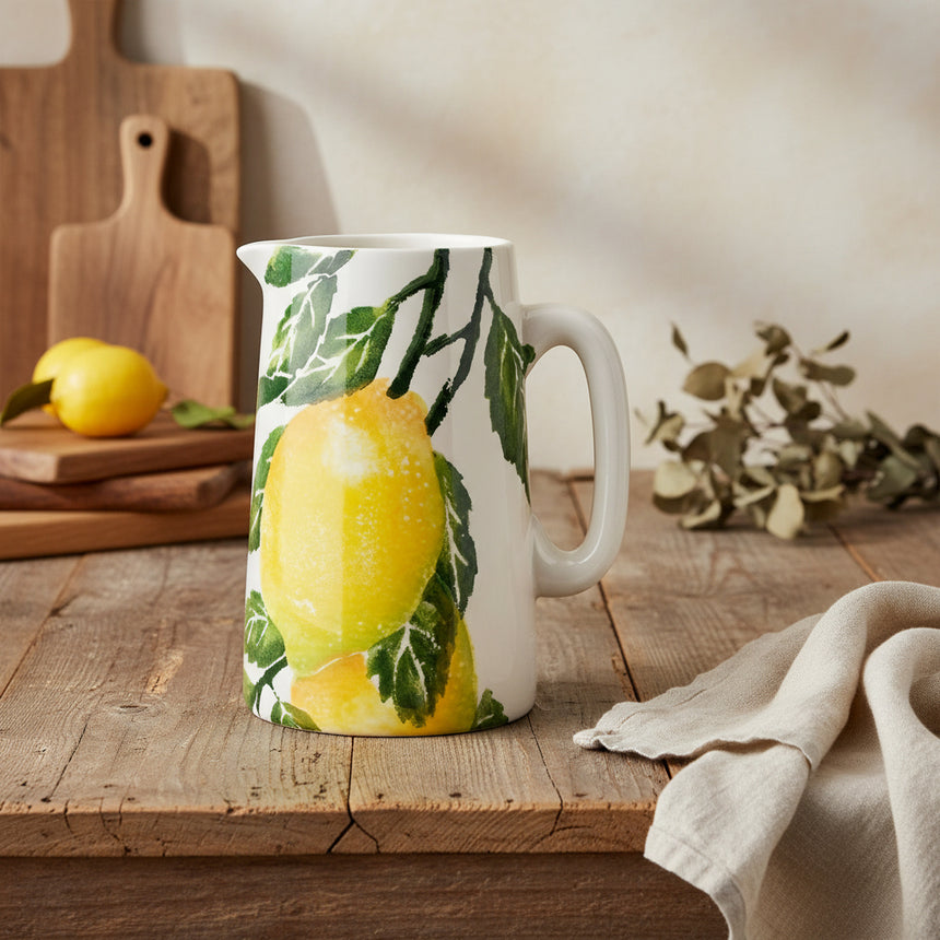 A ceramic water pitcher with a hand-printed illustration of bright Sicilian lemons on the vine, with a classic loop handle.
