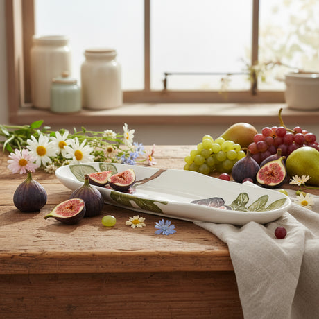 A shallow oval platter with a hand-printed illustration of fig fruits on a white background, with a leafy green border.