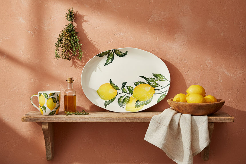 An oval white ceramic serving platter decorated with a watercolor-style print of yellow lemons on branches with green leaves, shown against a plain white background.
