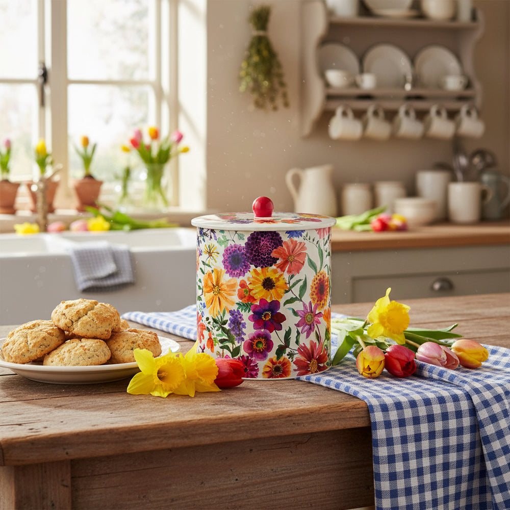A cylindrical stainless steel biscuit barrel with a floral pattern, featuring a variety of colorful flowers, and a red knob on the lid.
