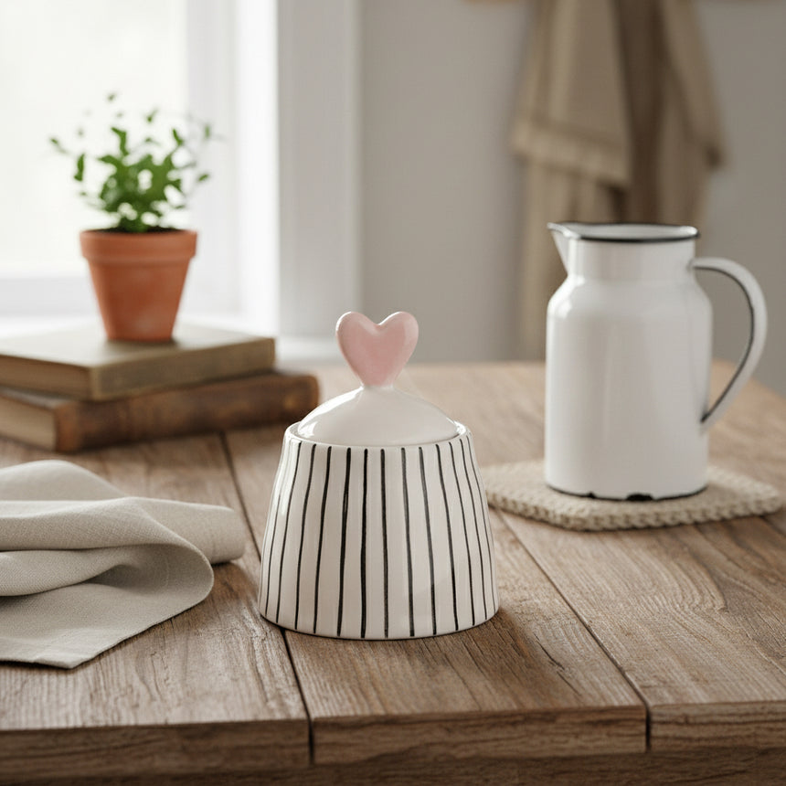 A white  sugar bowl with monochrome stripes design and a pastel pink heart-shaped lid on top, hand painted and glazed.