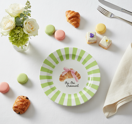 Round plate with green striped border and croissant illustration on a white background