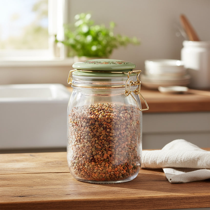A clear glass jar with a green metal lid and gold-tone wire bail closure, shown on a plain white background.