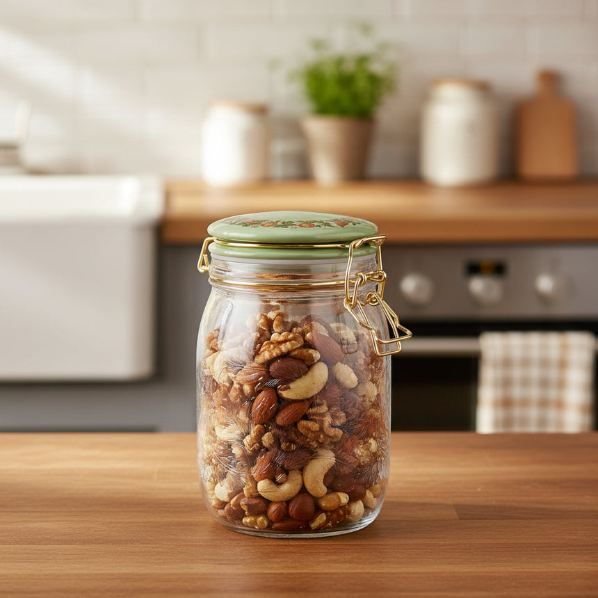 A clear glass jar with a gold metal clamp closure and a light green lid featuring a floral pattern, shown on a solid white background.