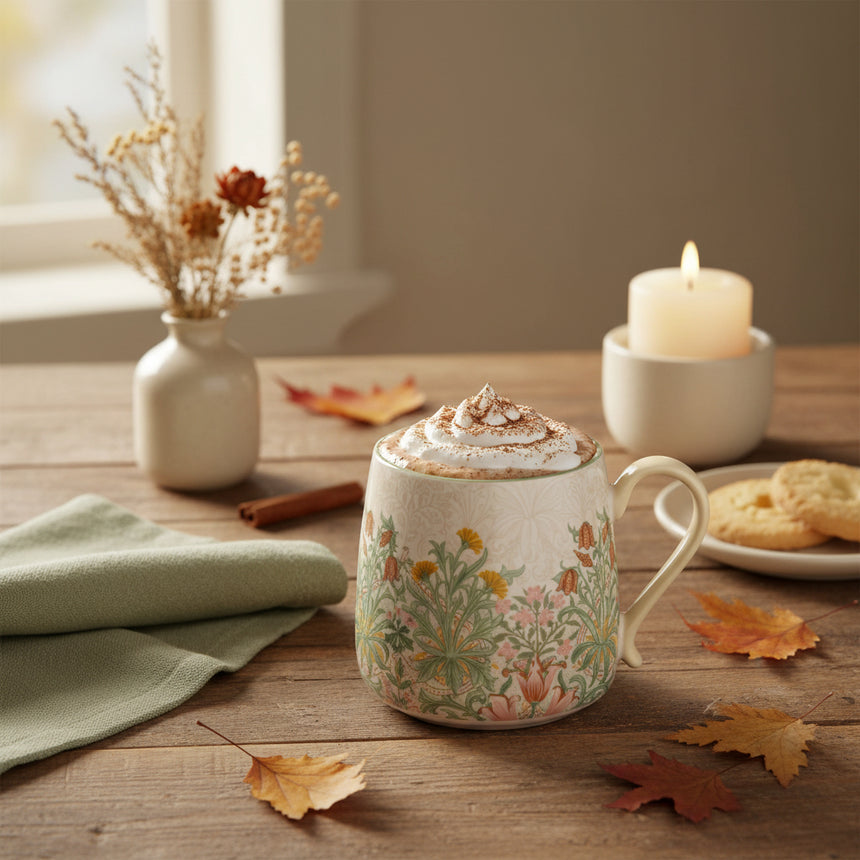 A ceramic mug featuring a light beige exterior decorated with a delicate green and orange botanical pattern, with a contrasting light green interior and a cream-colored handle.
