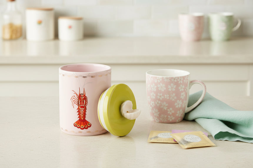 Pink ceramic container with a red lobster design and a yellow lid on a white background