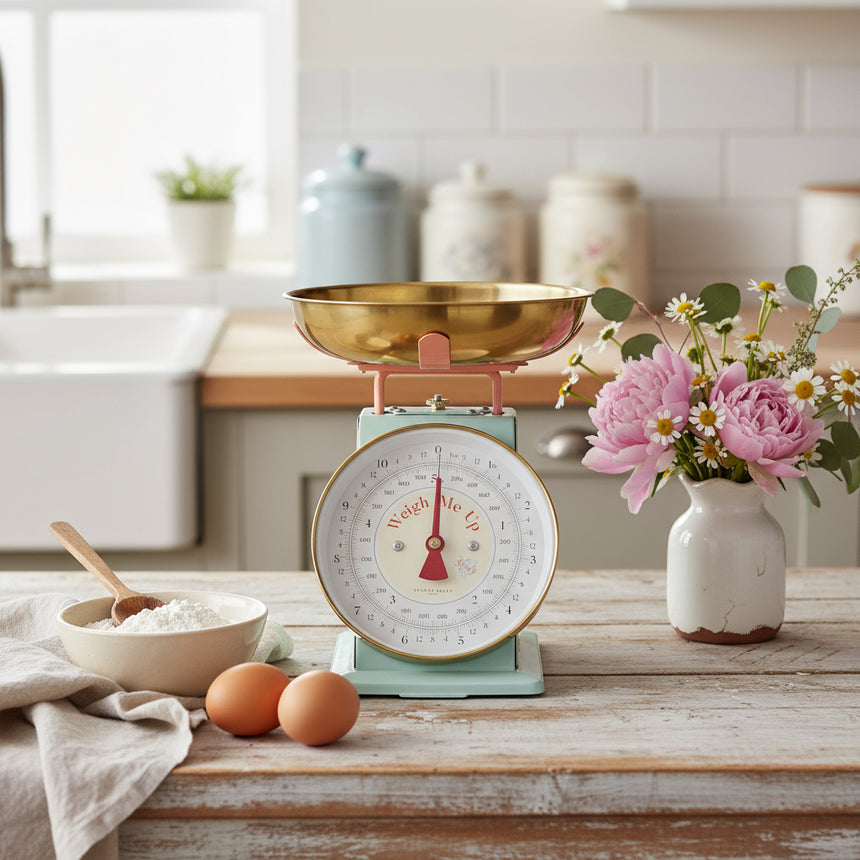 A mechanical kitchen scale with a pastel blue and pink body, brass finish, and a clear black on white dial.