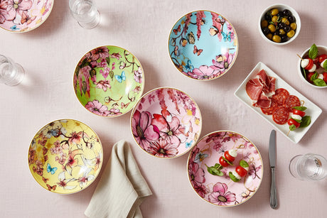 Four colorful ceramic bowls with floral and butterfly designs on a beige surface.