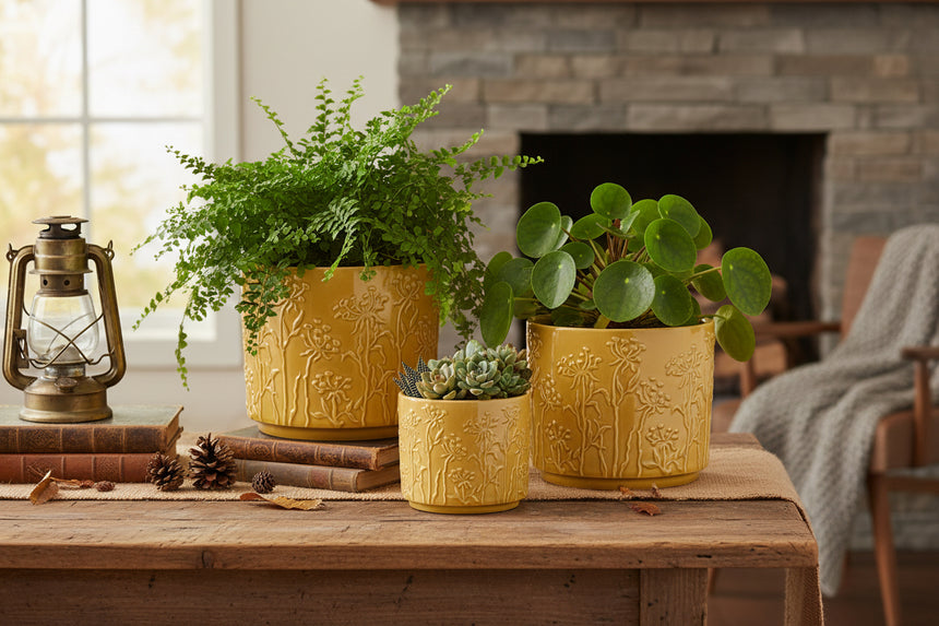 Set of three mustard yellow ceramic planters with floral patterns on a white background