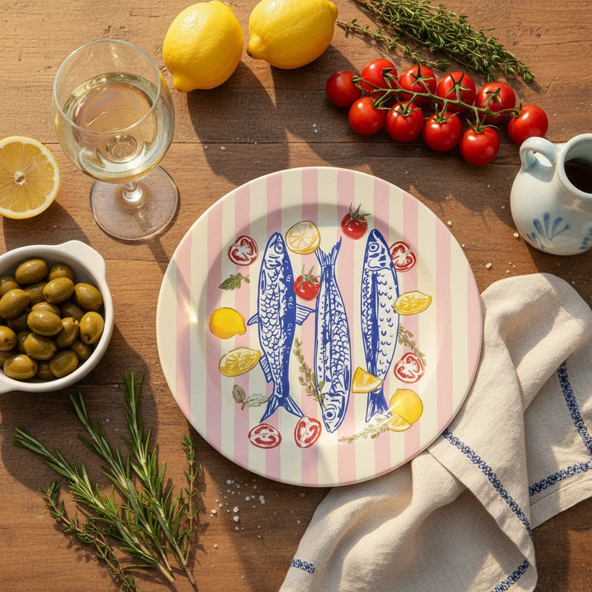 Round plate with blue fish, lemons, and tomatoes on a pink and yellow striped background
