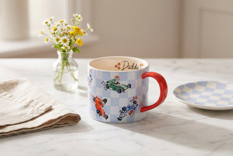 A white ceramic mug featuring a light blue and white checkered pattern with cartoon racing dogs in cars, a red handle, and the word 'Daddy' printed on the inside.