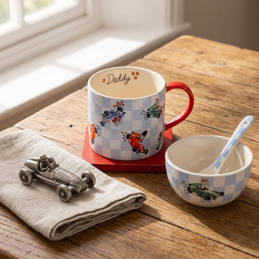 A white ceramic mug with a red handle, featuring a light blue and white checkered pattern with cartoon race cars and the word 'Daddy' printed inside.