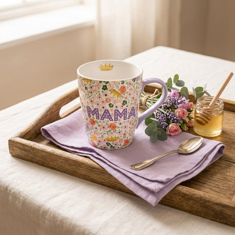 A white ceramic mug with a colorful floral pattern, featuring the word 'MAMA' in purple letters and a small gold crown motif, with a light purple handle.