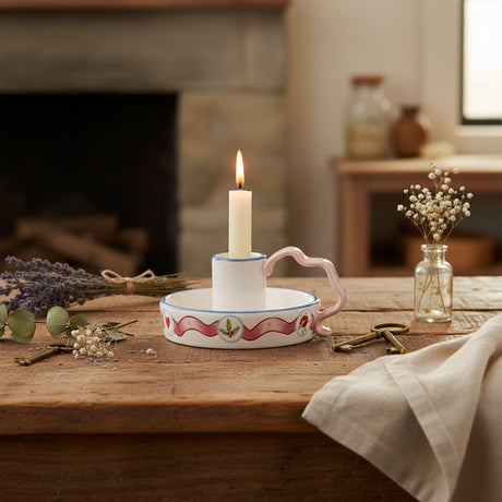 Decorative ceramic candle holder  with floral design and pink handle on a white background