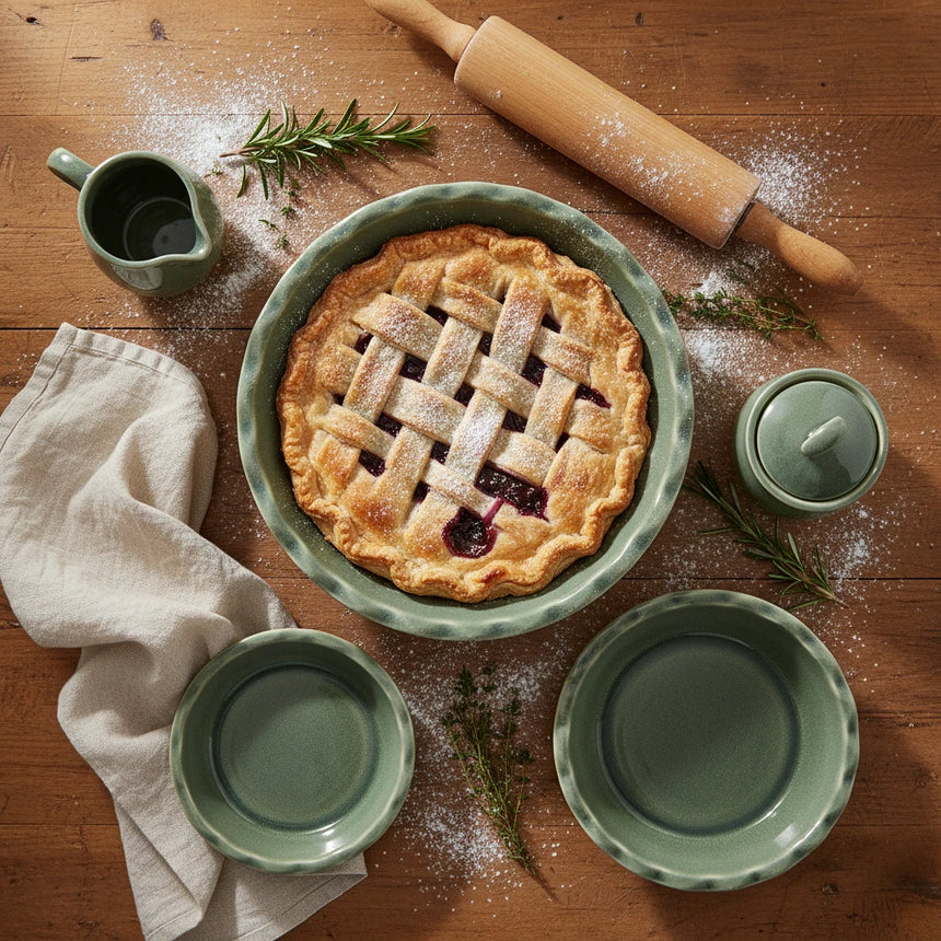 A top-down view of a  pie dish with a scalloped rim, featuring a matte sage green glaze on a white background.