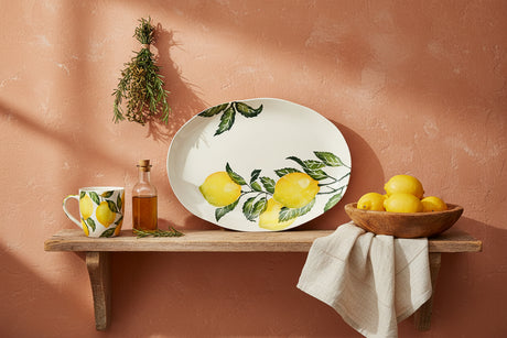 An oval white ceramic serving platter decorated with a watercolor-style print of yellow lemons on branches with green leaves, shown against a plain white background.