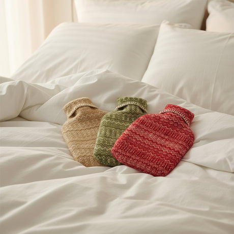 Three knitted hot water bottles in beige, green, and red on a white background