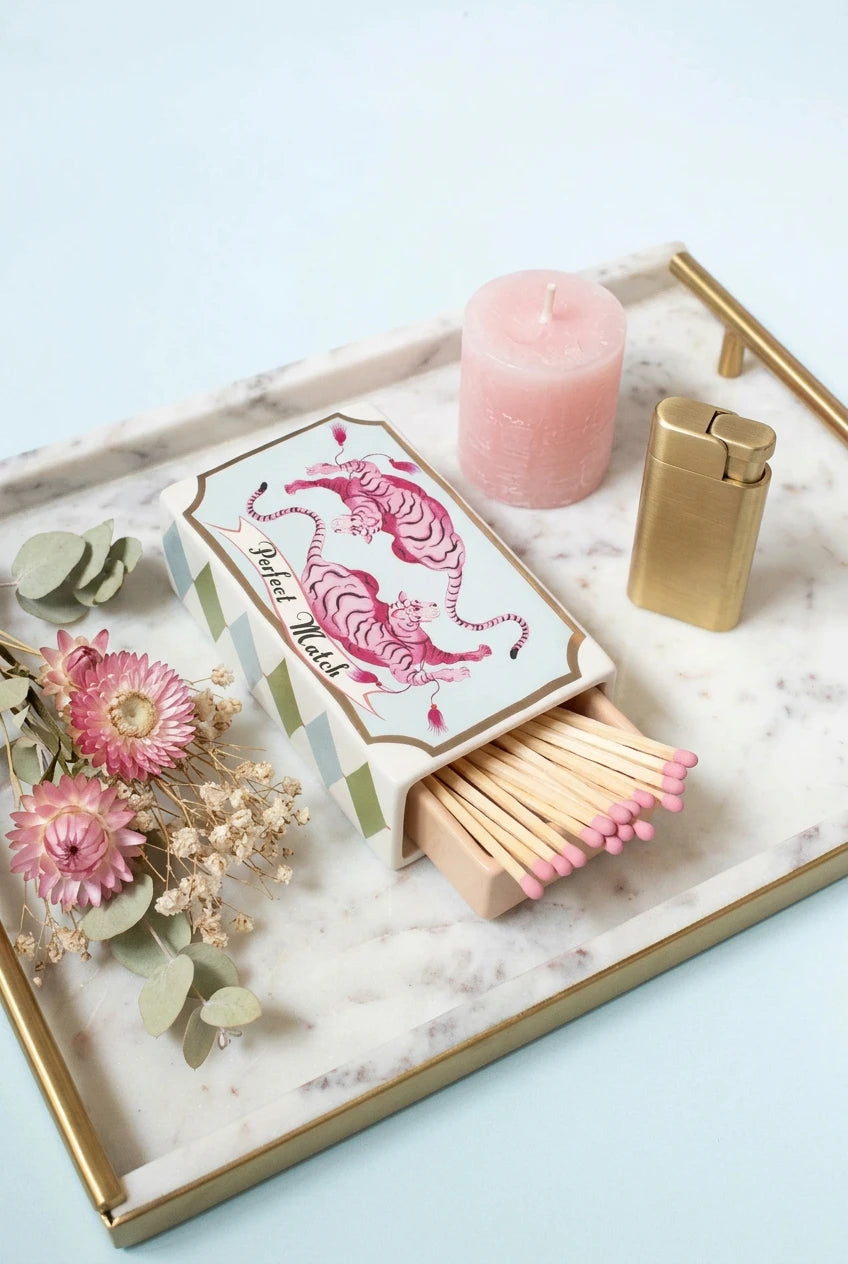 A small decorative ceramic matchbox with one drawer pulled open, shown on a pale blue background. The top lid features a pink tiger illustration and the words 'Arabian Nights,' while the sides have a white, green, and gold geometric pattern.