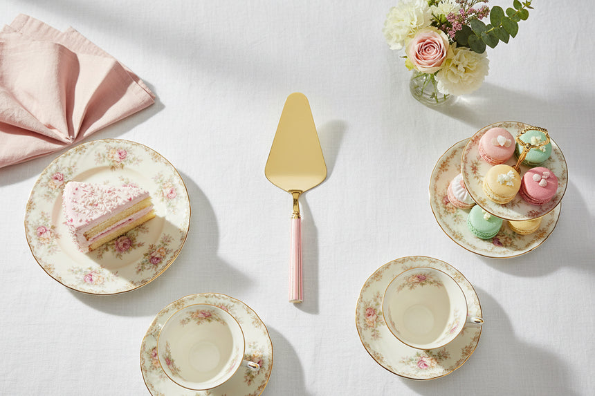 Gold cake server with pink handle on a white background