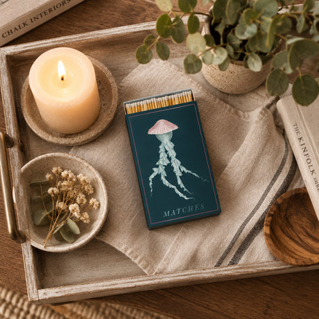 A matchbox package with a dark teal background featuring an illustration of a pale jellyfish and the word 'MATCHES' at the bottom. Wooden matchsticks with white tips are visible along the top edge, and the package is centered on a plain white background.