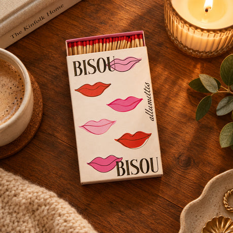 A matchbox package labeled 'BISOU' with illustrated pink and red lips and the word 'allumettes' printed vertically. The box is open, showing wooden matches with red tips arranged inside on a white background.
