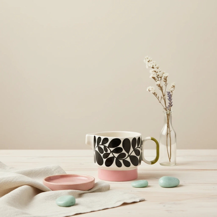 Ceramic mug with black leaf pattern and pink base on a light beige background
