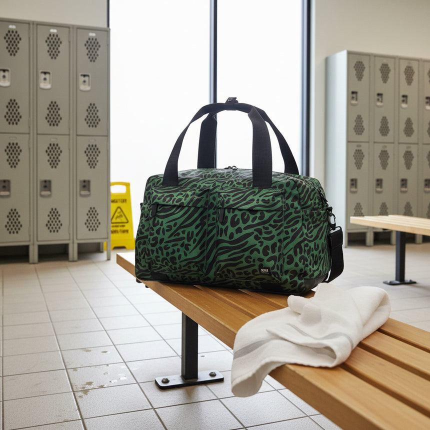 A green and black animal-print duffel bag with black webbed handles, shown on a plain white background.