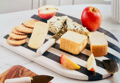 Cheese platter with various types of cheese, crackers, and apples on a marble surface.