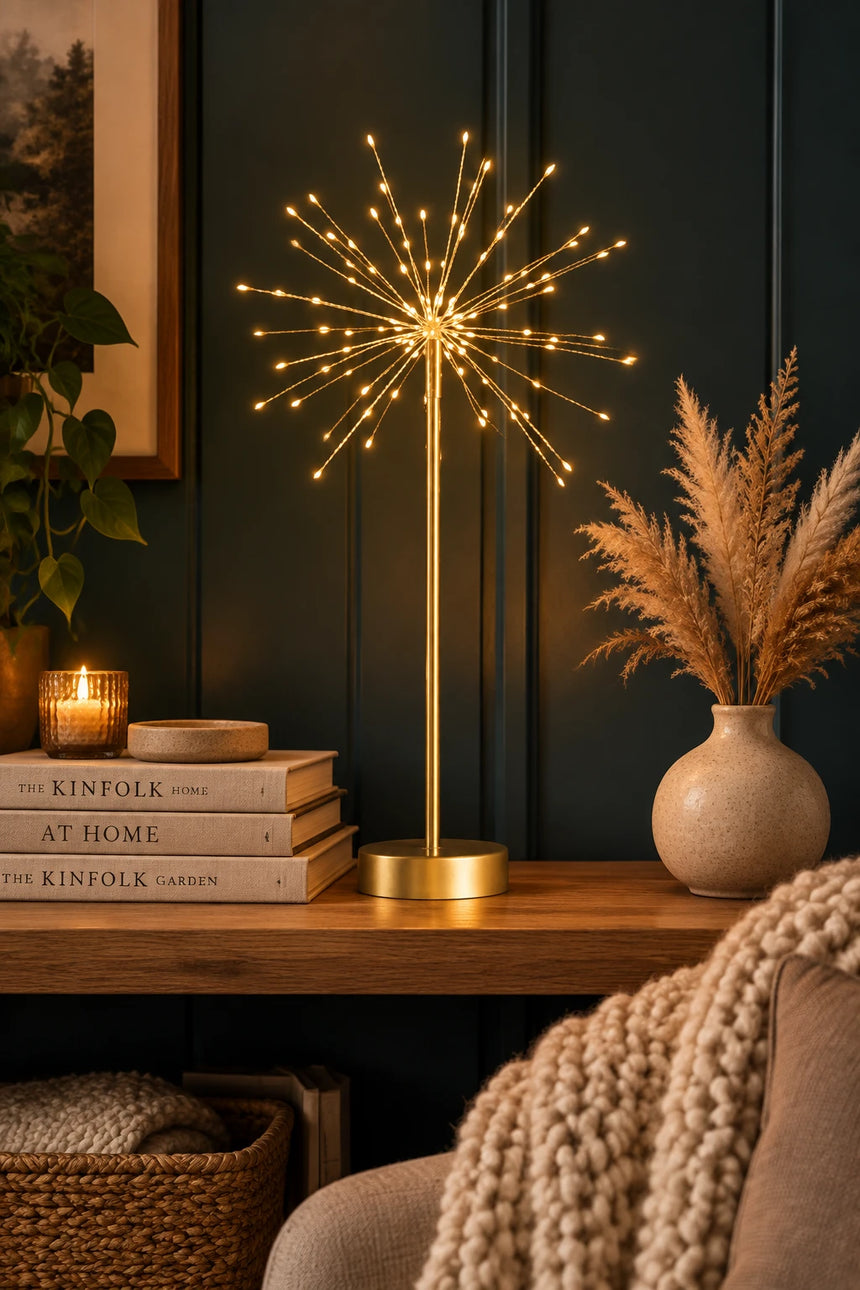 A gold table lamp with a spherical starburst wireframe design and warm glowing LED lights, set against a dark paneled background.