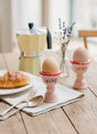 Two eggs in pink holders labeled 'MINE' and 'YOURS' on a kitchen counter.