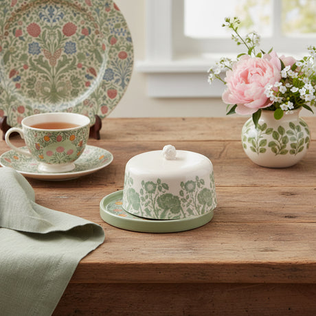 A small ceramic butter dish with a matching lid, featuring a pale pink upper section with a green floral pattern and a muted sage green base with a colorful floral rim.
