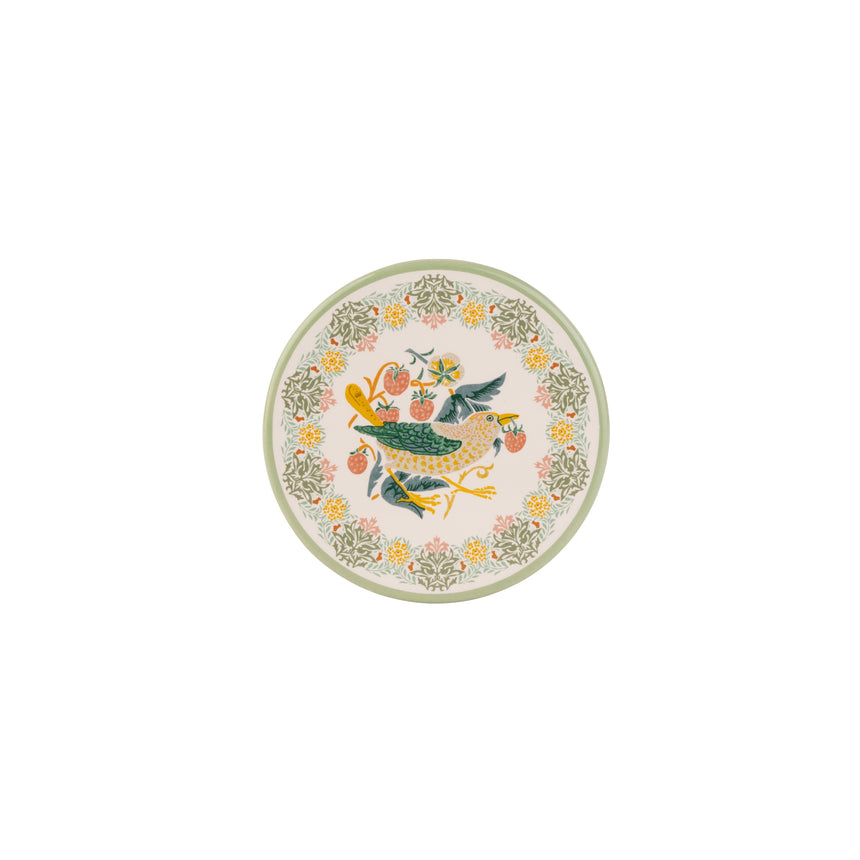 A round ceramic coaster with a light pink background, featuring a central illustration of a green bird holding a yellow flower, surrounded by a border of yellow and pink flowers and green leaves.