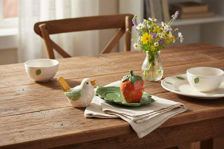 A ceramic bird and strawberry salt and pepper shaker set on a white background. The bird is white with a green wing, yellow beak, and brown tail.