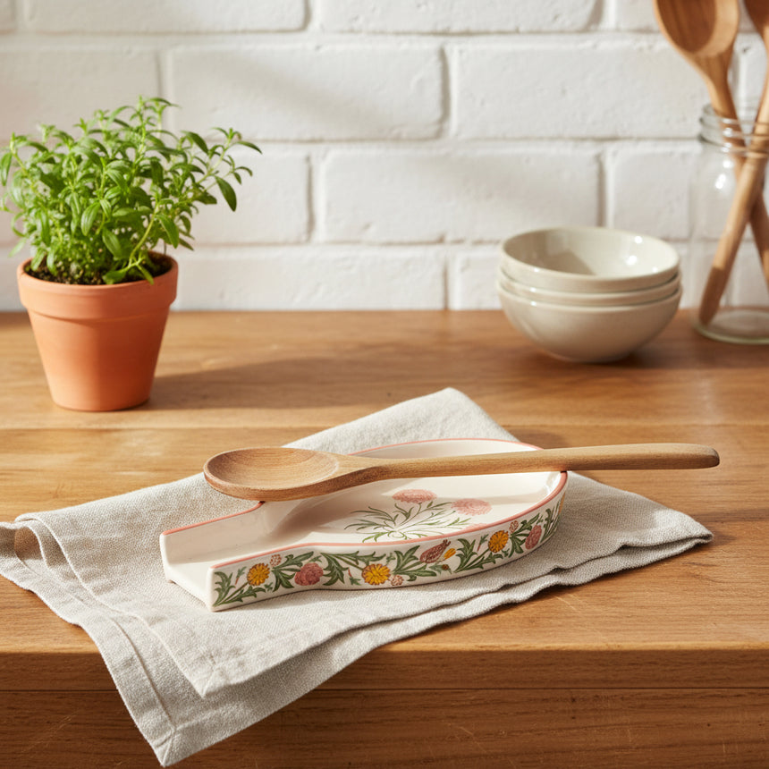 A small ceramic SPOON REST , featuring a pink floral pattern on the interior and a green botanical border on the exterior, set against a plain white background.