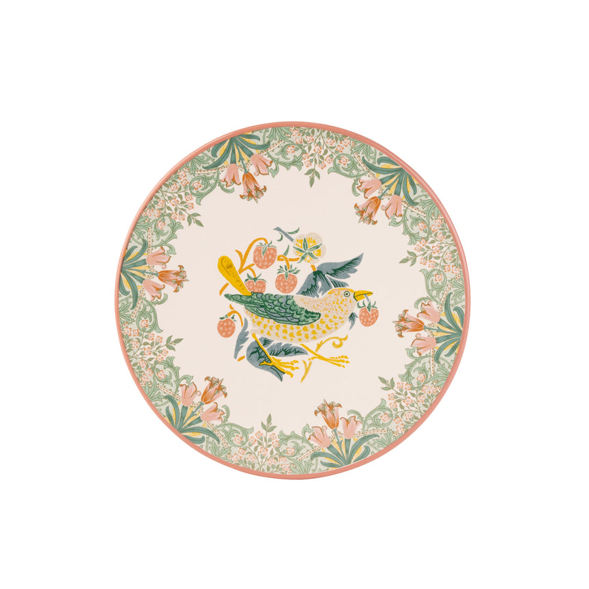 A round decorative trivet featuring a central bird motif in green, yellow, and blue, surrounded by a floral border in soft pink, green, and cream on a white background.