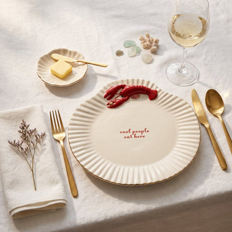 A white ceramic sea shell shaped serving plate with a red lobster decoration on the top right and the red text 'cool people eat here' printed in the center, set against a plain white background.