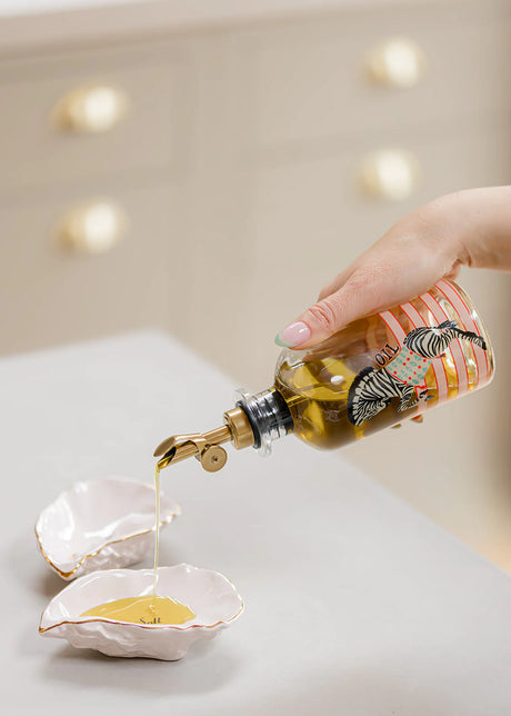 Person pouring oil from a decorative bottle into oyster shells on a light surface.