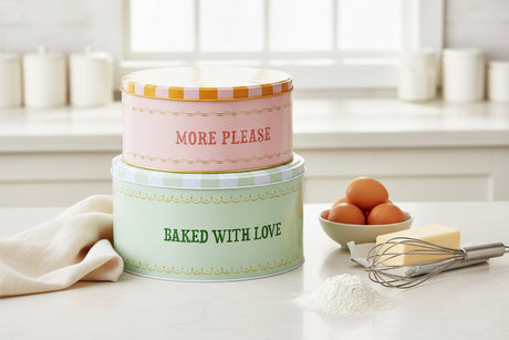 Two-tiered cake-shaped tin with 'More Please' and 'Baked with Love' text on a white background