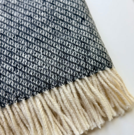 Close-up of a woven textile with a dark charcoal and off-white cream fringe 