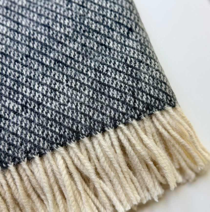 Close-up of a woven textile with a dark charcoal and off-white cream fringe 